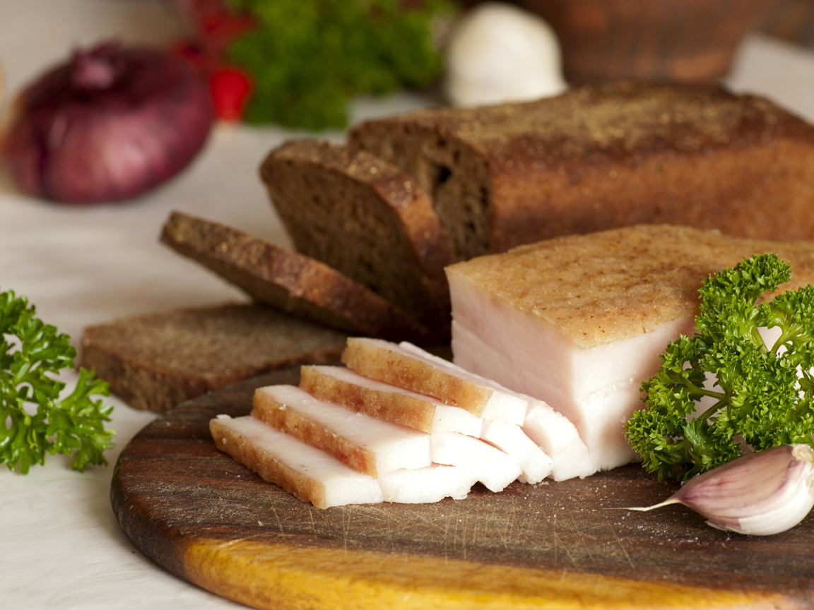 Нарезанное кусочками сало и черный хлеб на разделочной доске