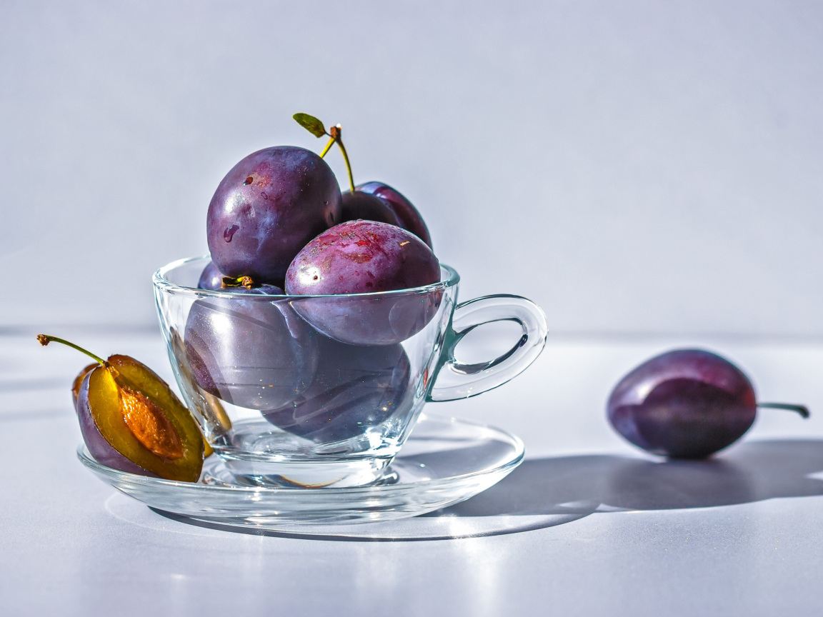 Спелые синие сливы на столе в стеклянной чашке