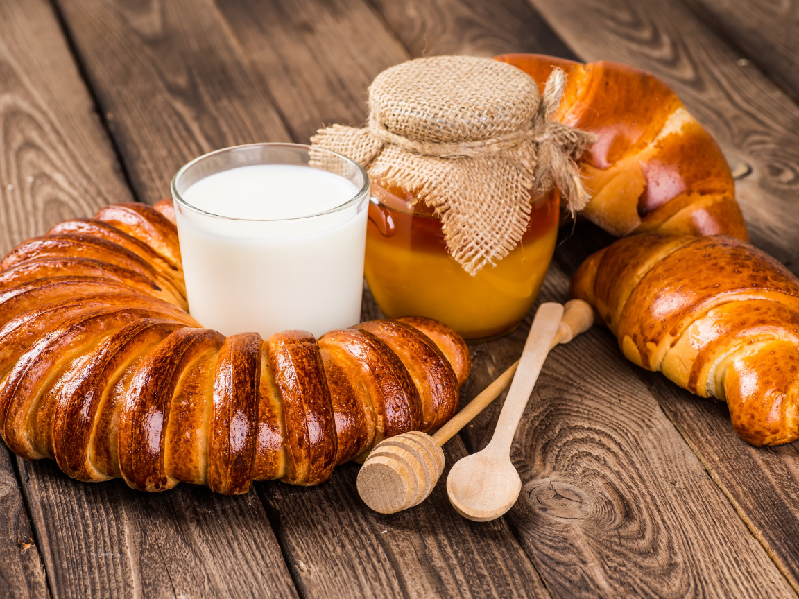 Свежая выпечка на столе со стаканом молока и медом