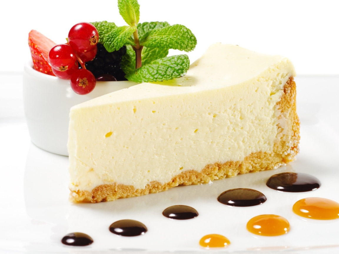 Кусок чизкейка на белой тарелке с ягодами и мятой