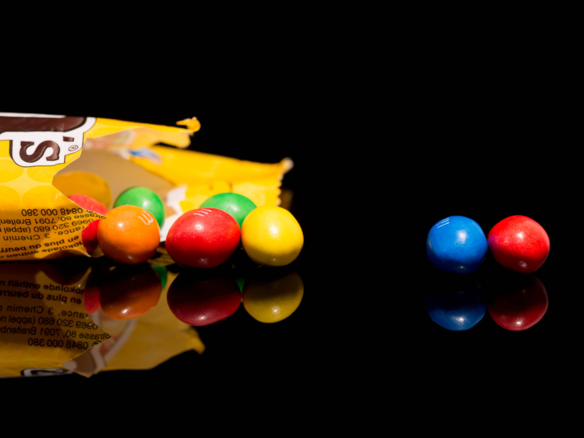 Разноцветные конфеты  M&m's отражаются в черной поверхности стола 