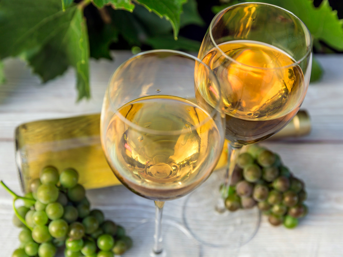 Два бокала белого вина с белым виноградом на столе