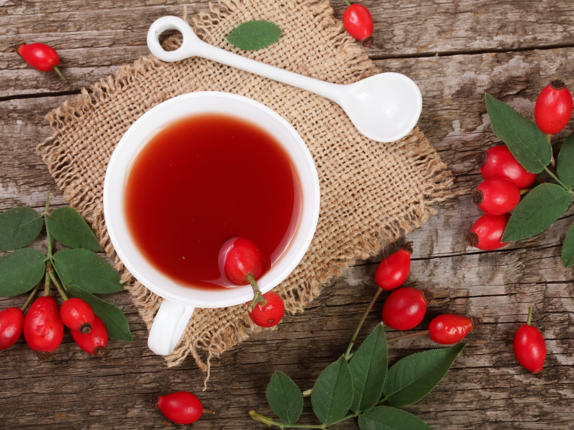 Белая чашка чая с ягодами шиповника на столе