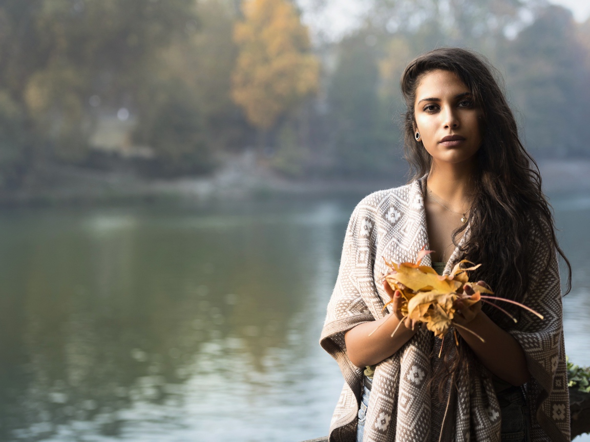 Красивая брюнетка у реки с желтыми листьями в руках