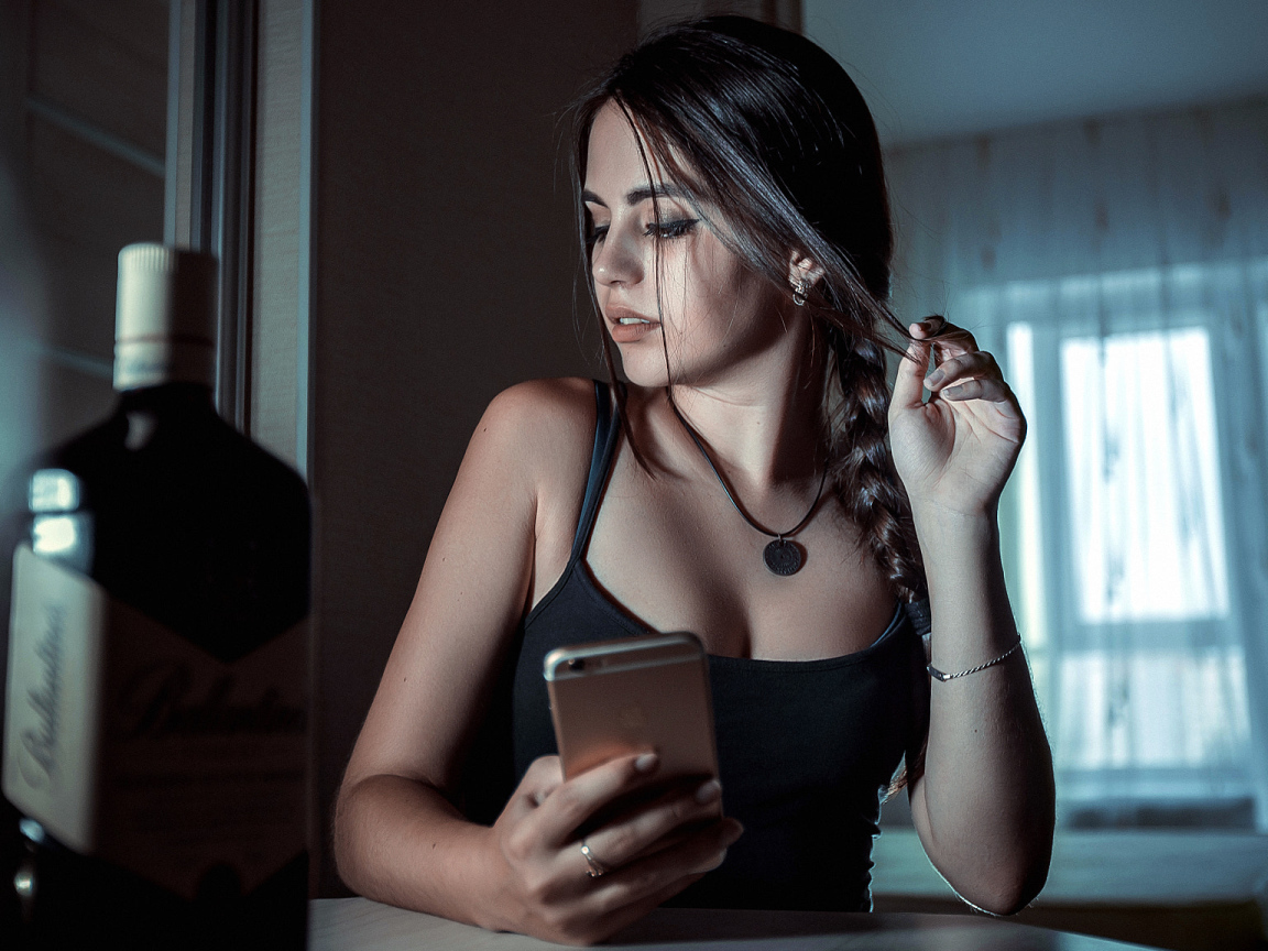 Красивая брюнетка с телефоном в руках и бутылкой