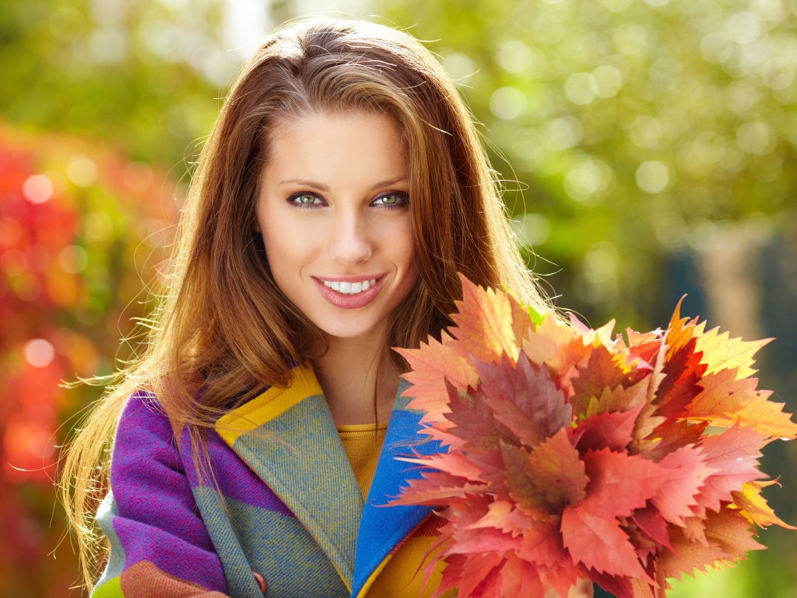 Красивая улыбающаяся девушка с букетом желтых листьев в руке