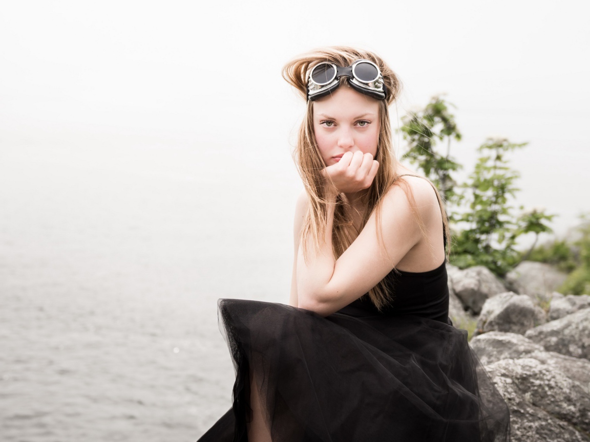 Девушка блондинка с очками на голове сидит на камне