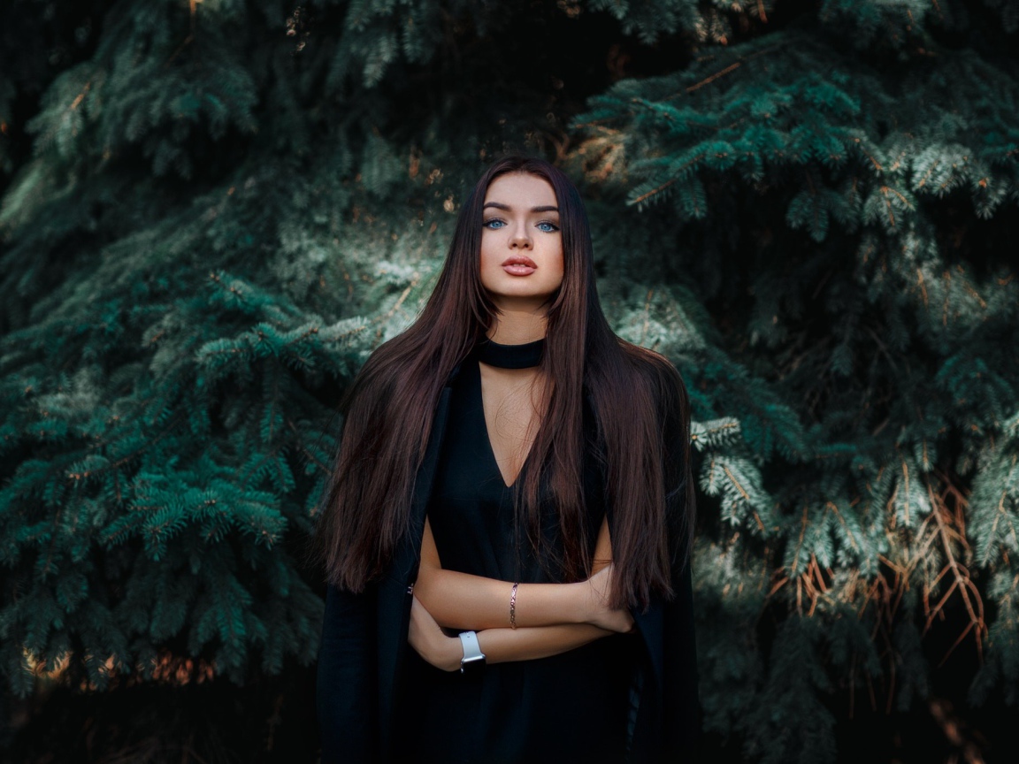 Голубоглазая девушка брюнетка у большой зеленой ели 