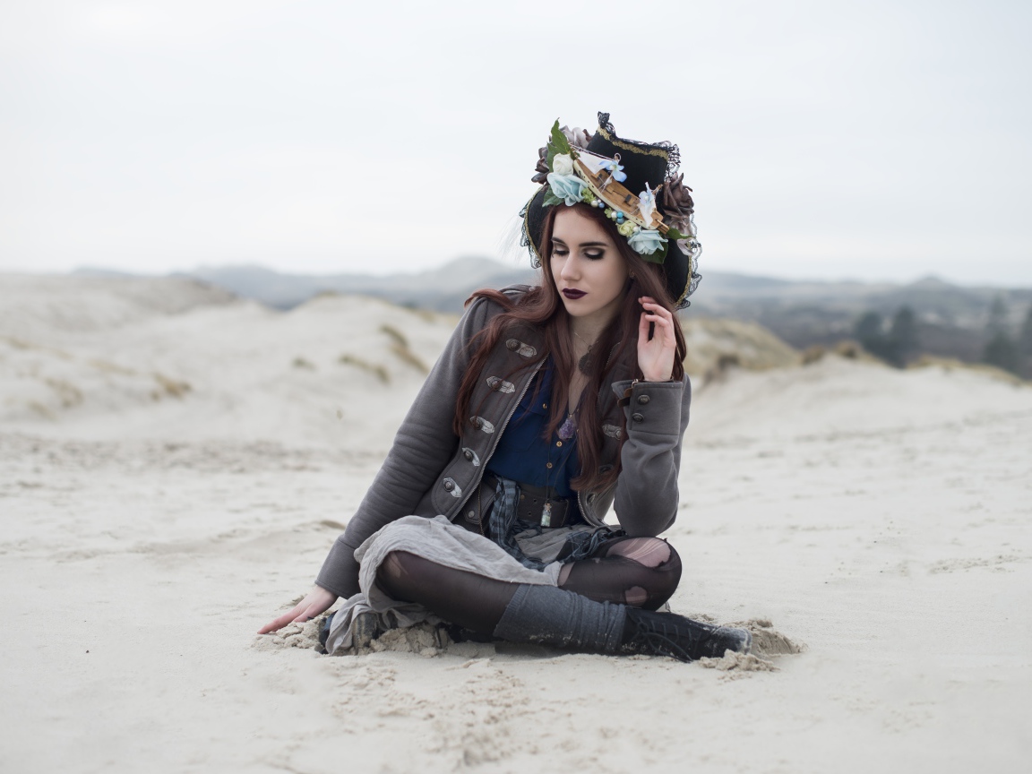 Девушка брюнетка  в костюме сидит на песке 