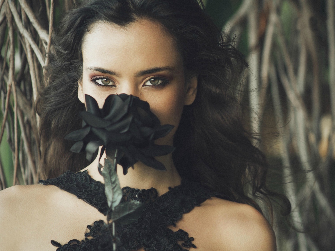 Green-eyed brunette girl with black rose in hands