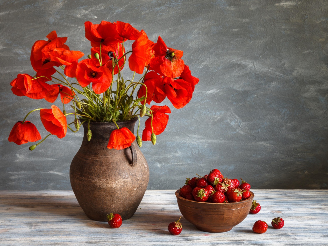 Красивый букет красных полевых маков в вазе на столе с клубникой