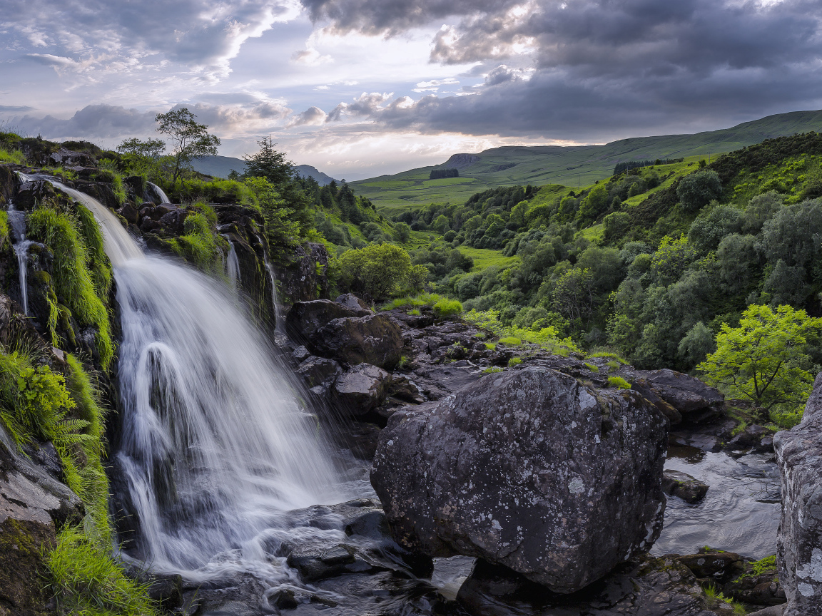 Водопад стекает по камням на фоне красивого неба и зеленого леса