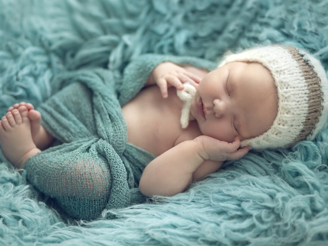 Грудной ребенок спит на зеленом меховом покрывале