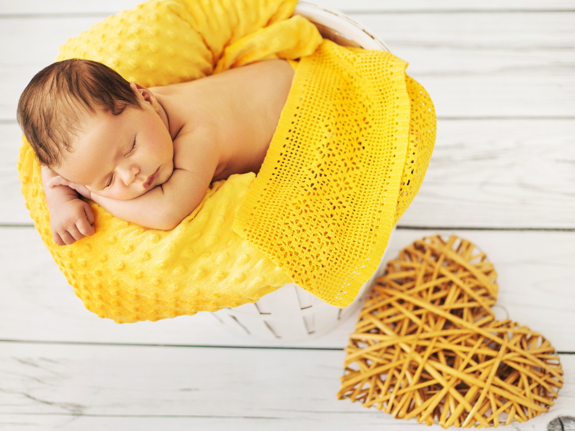 Грудной ребенок спит на желтой подушке с плетеным сердцем