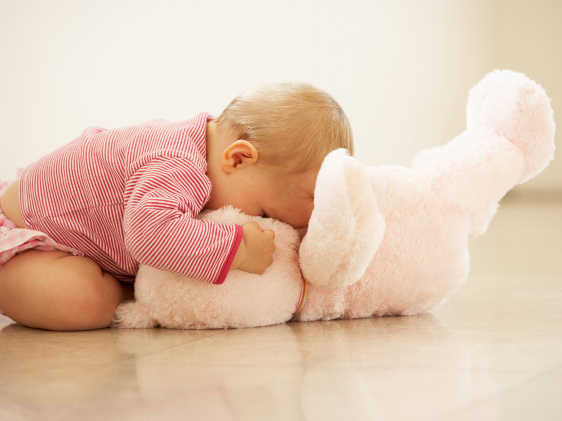 Маленький ребенок играет с розовым игрушечным медведем