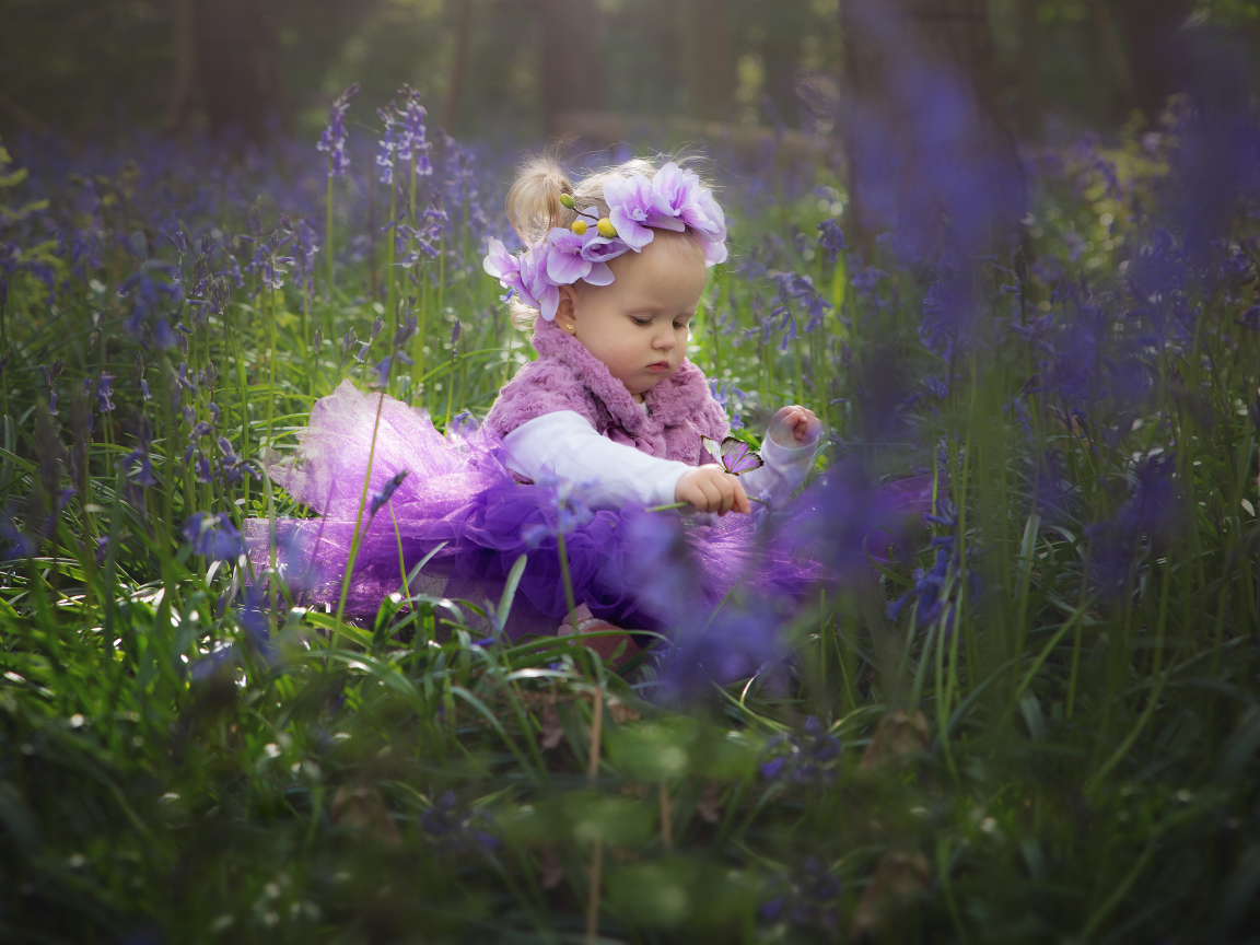 Маленькая девочка в красивом платье сидит в цветах с бабочкой на руке