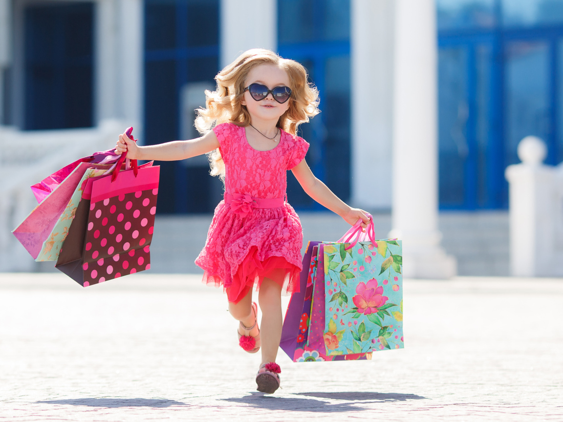 Маленькая девочка в розовом платье бежит с покупками из магазина