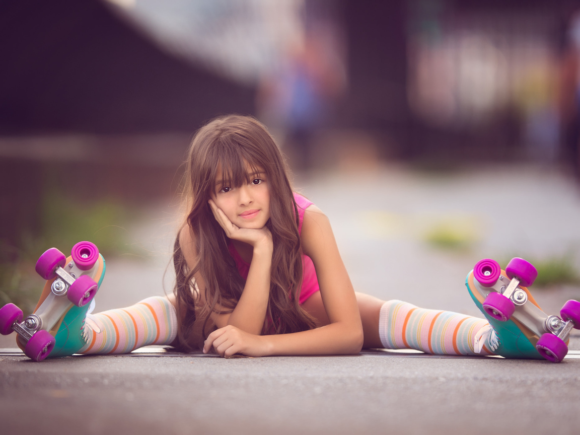 Маленькая девочка сидит на дороге в роликах