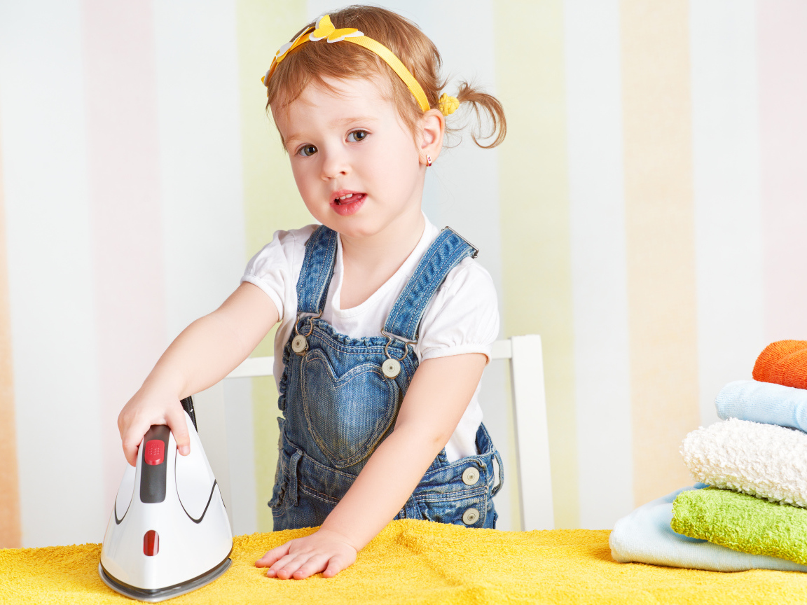 Маленькая девочка с утюгом гладит полотенце