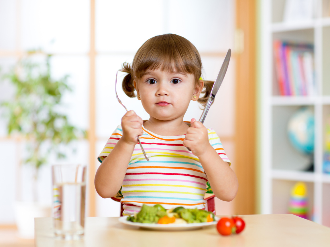 Маленькая девочка со столовыми приборами и тарелкой