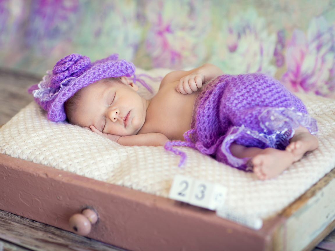 A little sleeping baby in a knitted purple suit