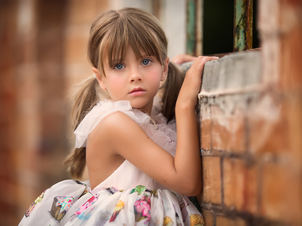 Милая девочка с серьезным взглядом стоит у стены