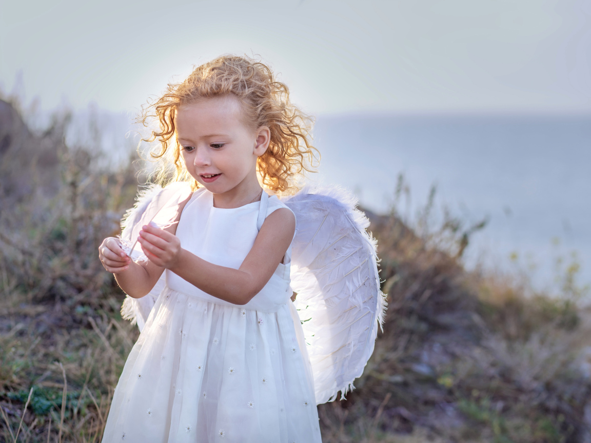 Красивая маленькая девочка в белом платье с крыльями ангела