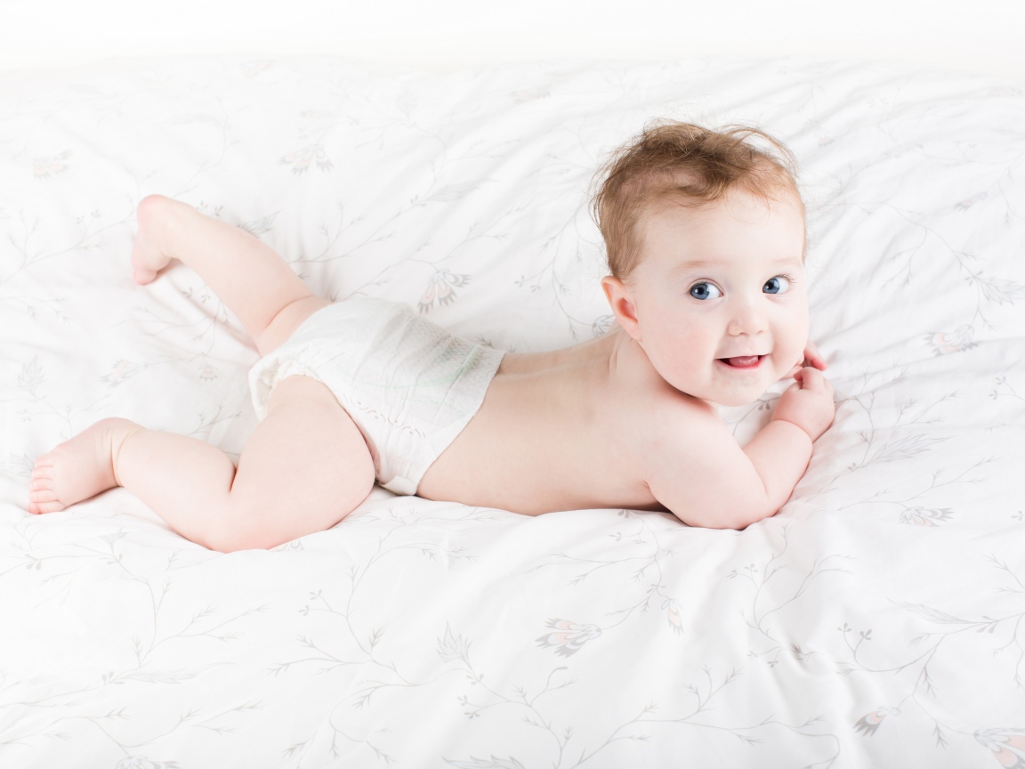 Забавный голубоглазый малыш лежит на белом покрывале