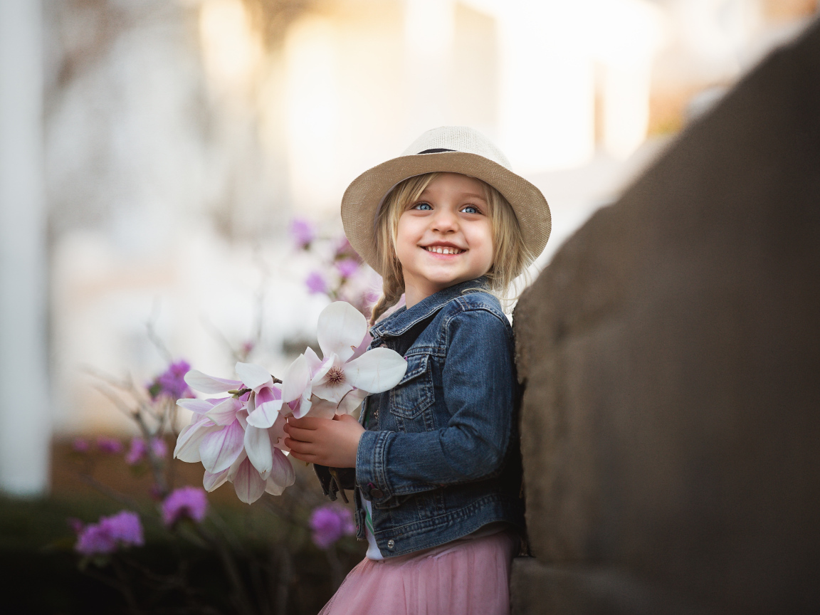 Маленькая голубоглазая улыбающаяся девочка в шляпе с букетом в руках