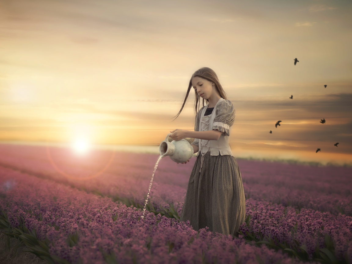 Маленькая девочка поливает цветы из кувшина в поле на закате