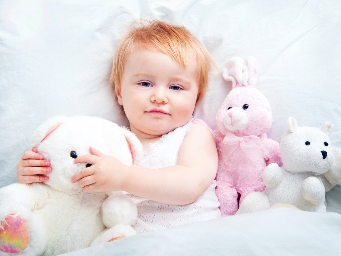 Маленькая девочка лежит в кровати с плюшевыми игрушками