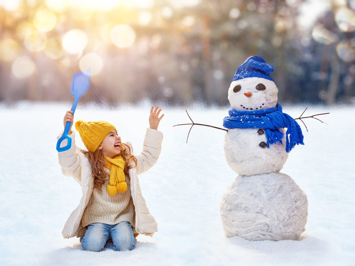 Маленькая улыбающаяся девочка со снеговиком зимой