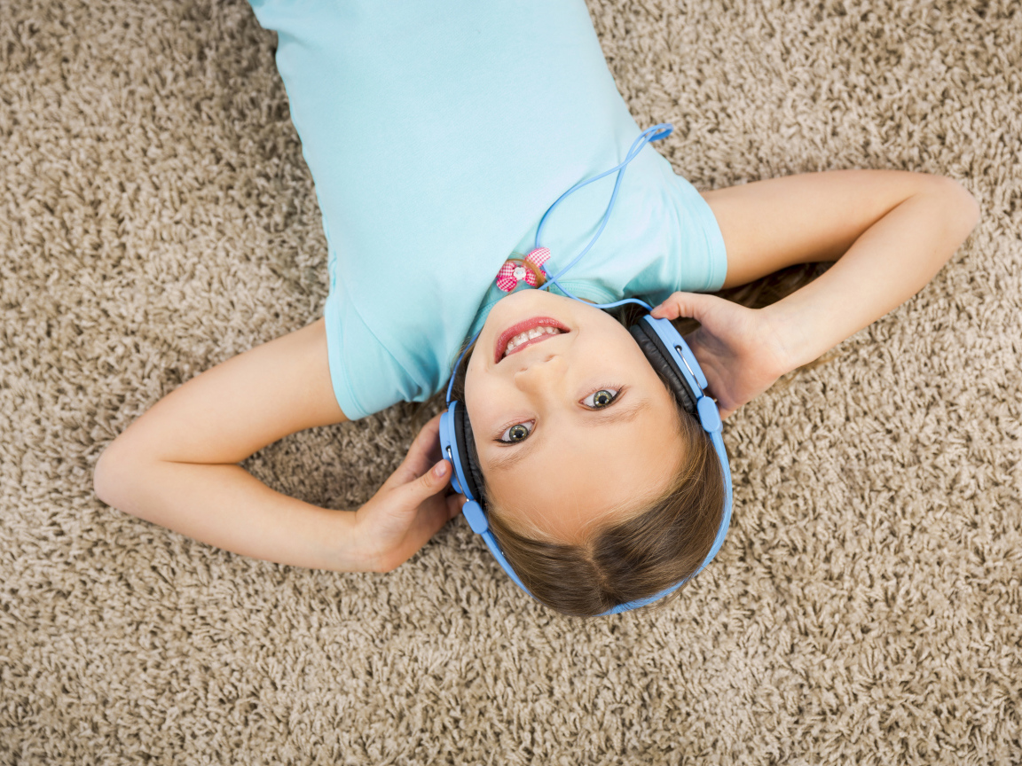 Улыбающаяся девочка в больших голубых наушниках