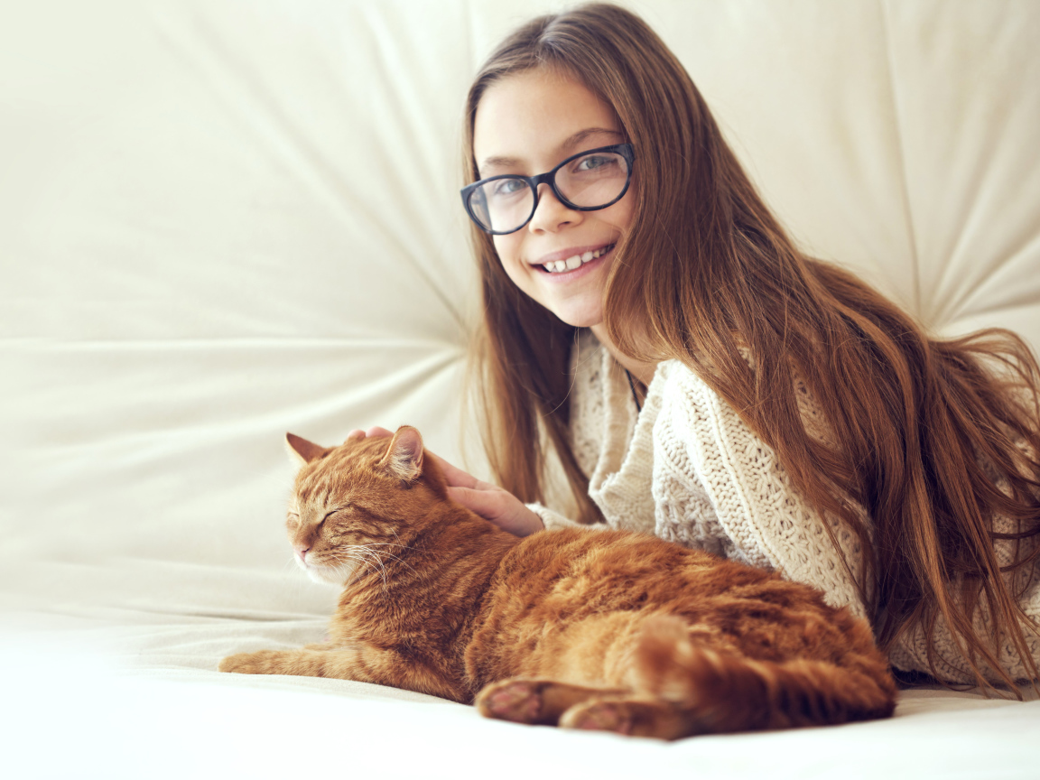 Улыбающаяся девочка шатенка в очках гладит рыжего кота