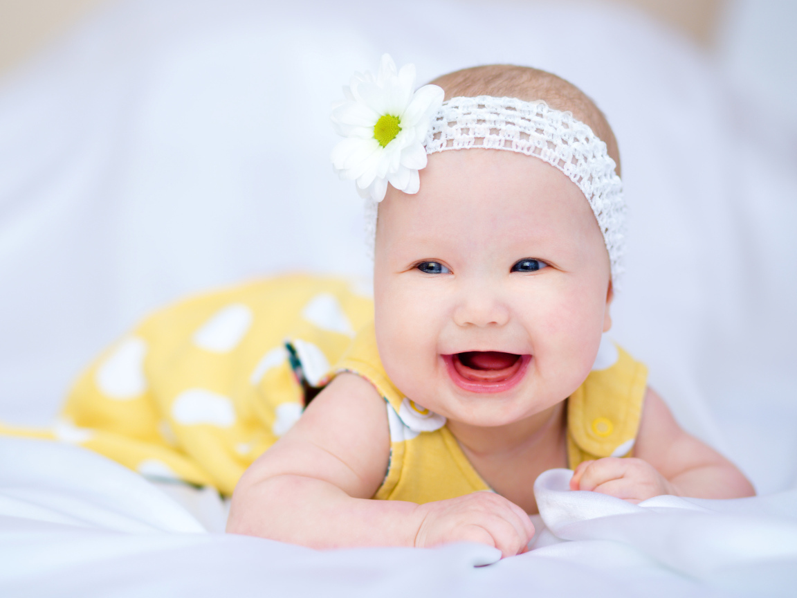 Улыбающаяся маленькая девочка в повязке с белым цветком на голове