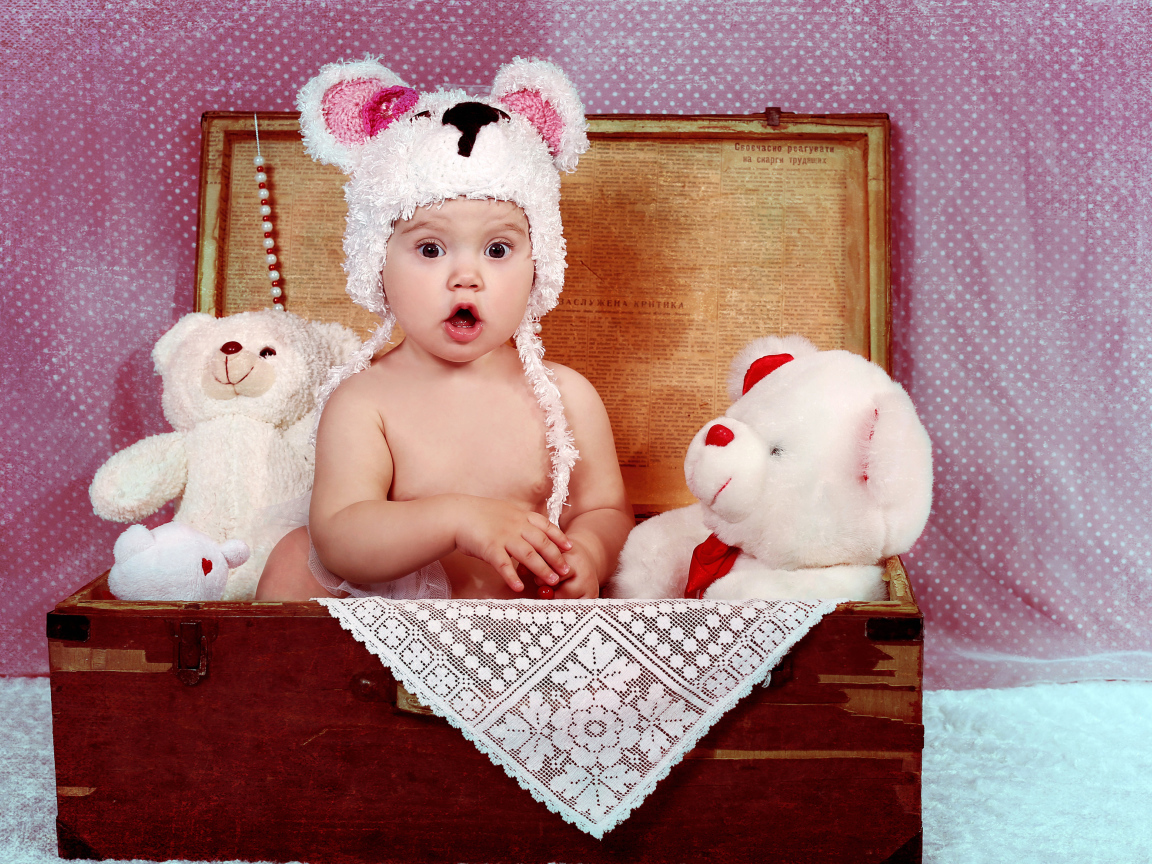 Удивленный малыш сидит в сундуке с мягкими игрушками