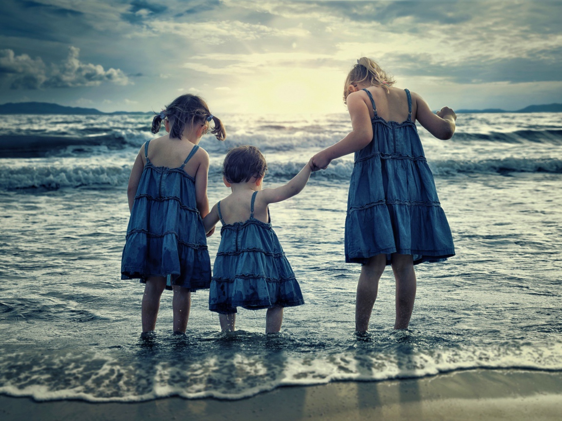 Три маленькие девочки стоят в воде на берегу моря