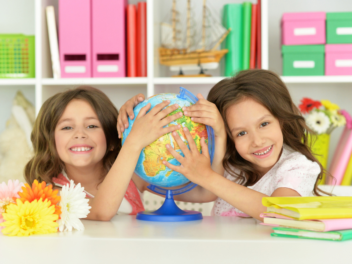 Две маленькие девочки школьницы с глобусом  в руках