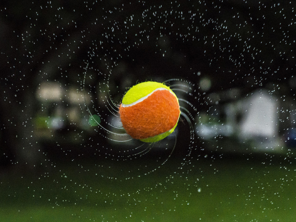 Теннисный мяч летит в каплях воды 