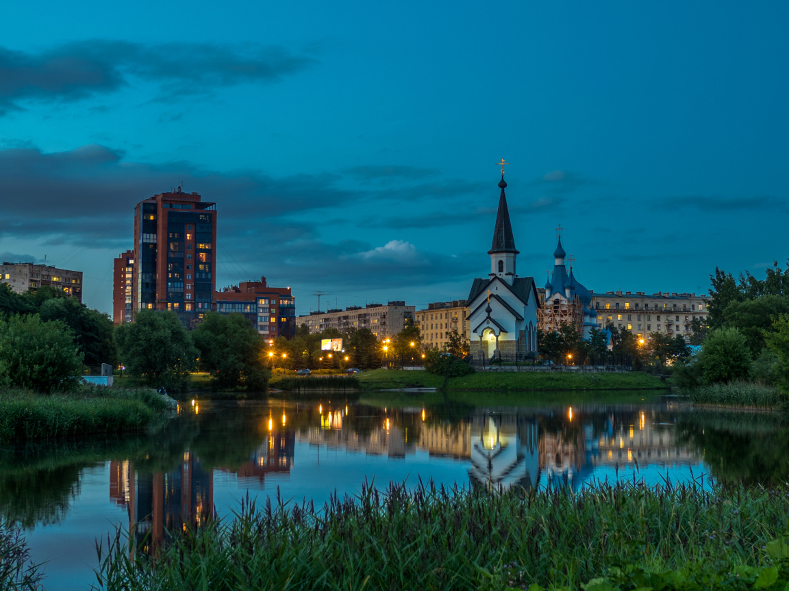 Вечерние огни маленькой церкви и домов отражаются в воде городского пруда, Санкт-Петербург. Россия
