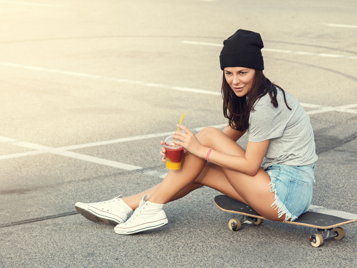 Спортивная девушка сидит на доске для скейтборда 