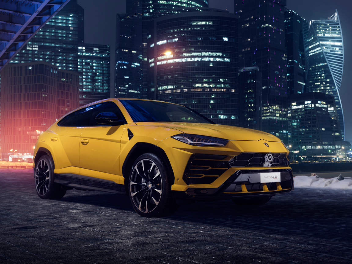 Желтый Lamborghini Urus на фоне ночных небоскребов