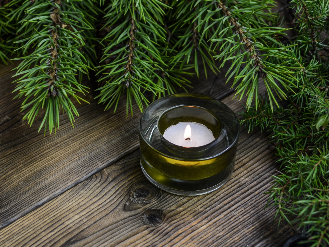 Зажженная свеча на столе с зеленой веткой ели