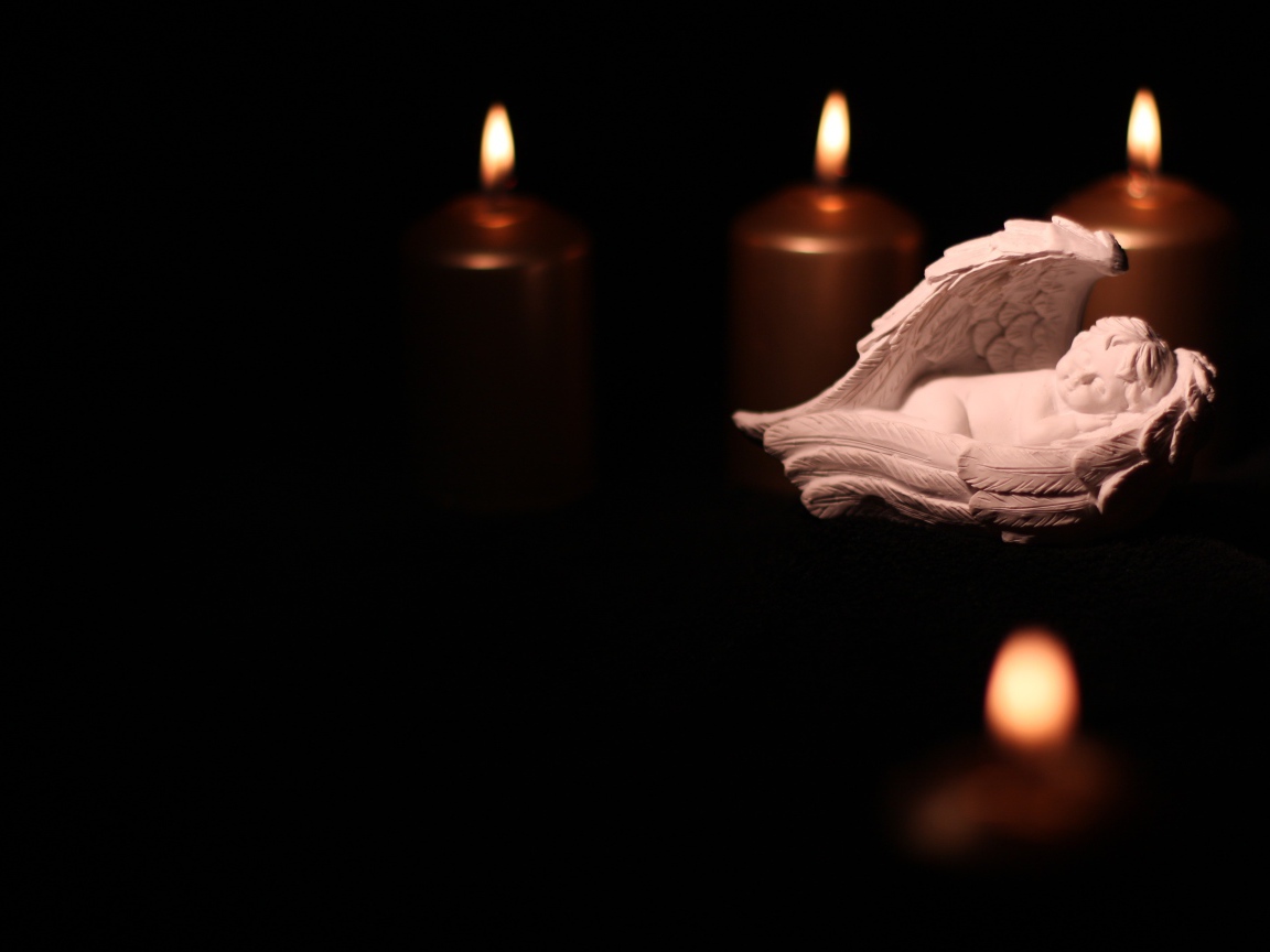 Фигурка ангела освещен горящими свечами на черном фоне