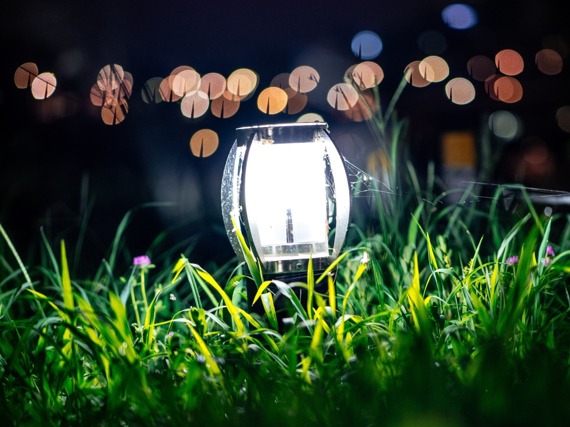 Включенный фонарь стоит в зеленой траве