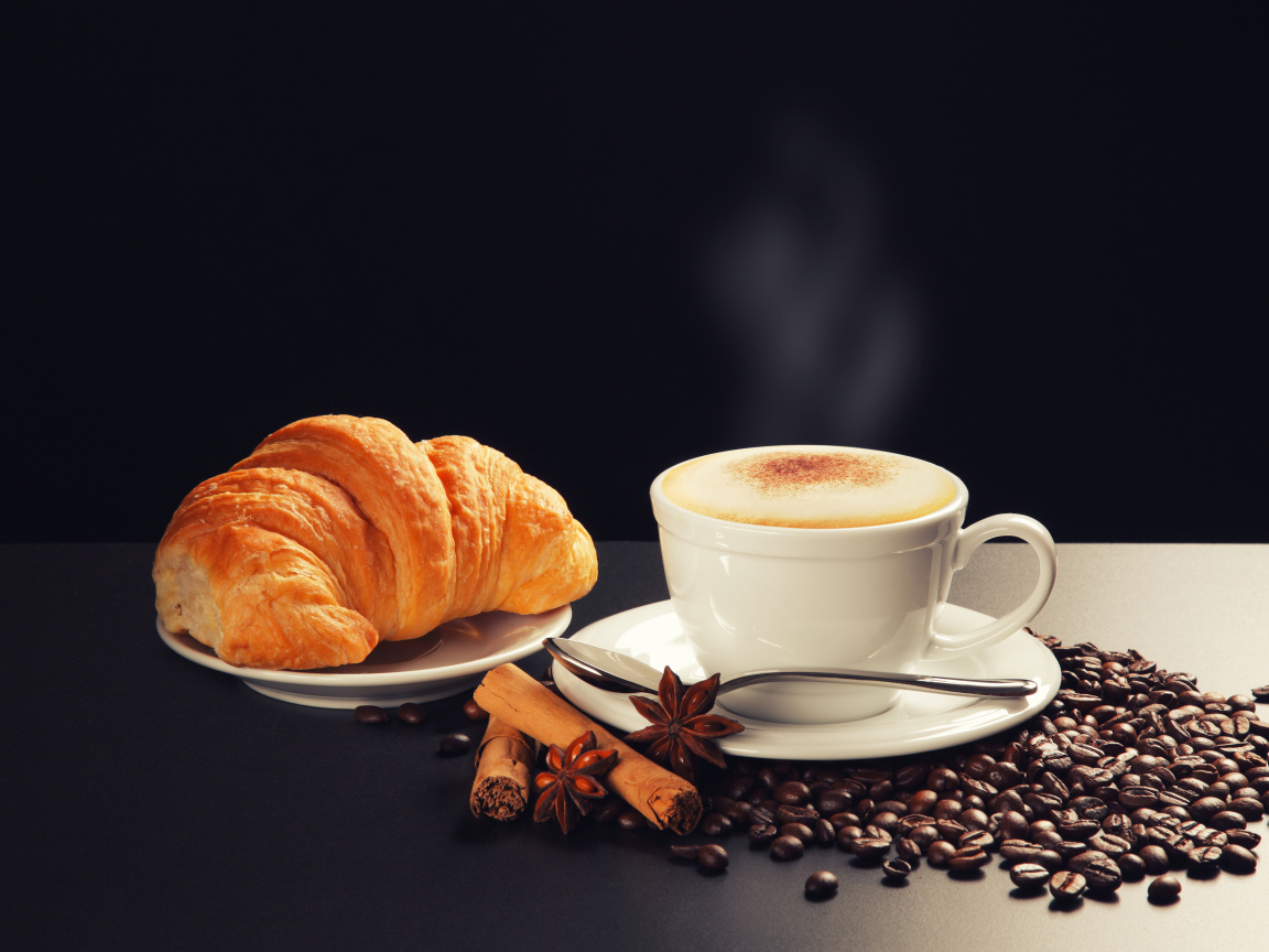 A cup of coffee on the table with coffee beans, star anise, cinnamon croissant