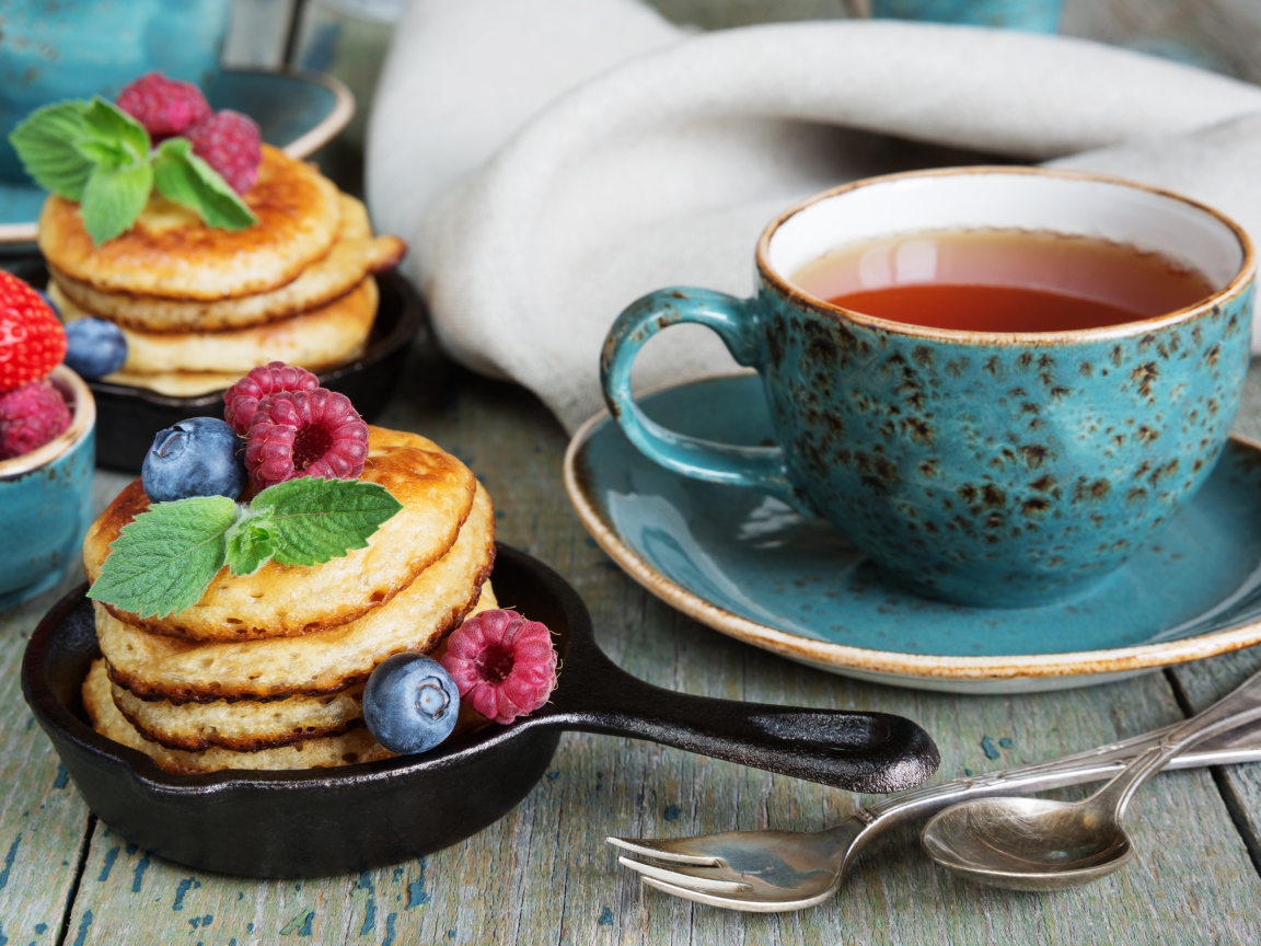 Чашка чаю с оладьями с ягодами на столе