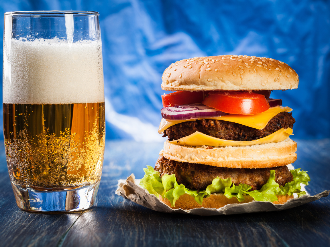 Стакан пива с гамбургером на столе