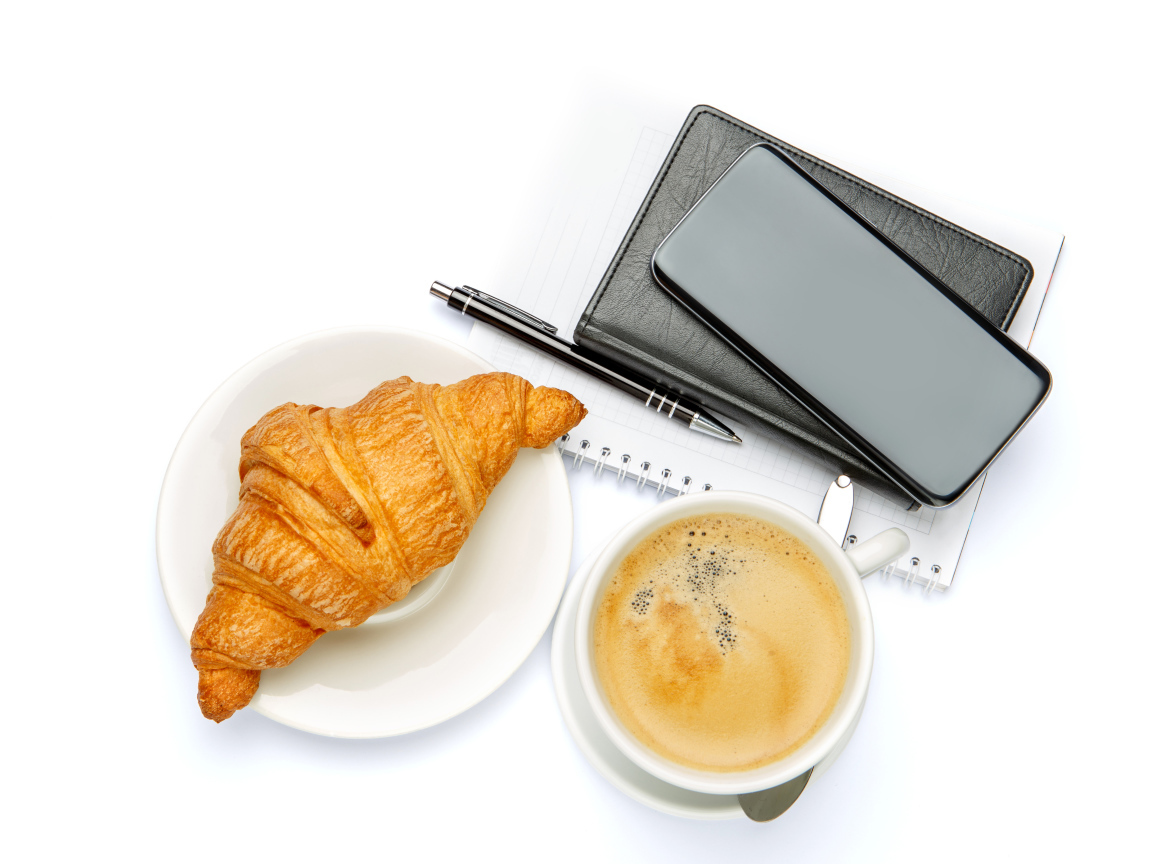 Чашка кофе, круассан, блонтон и смартфон на белом 