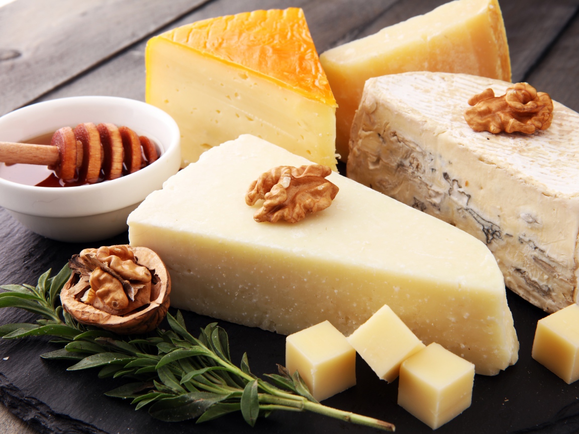 Разные виды сыра на столе с медом и грецкими орехами